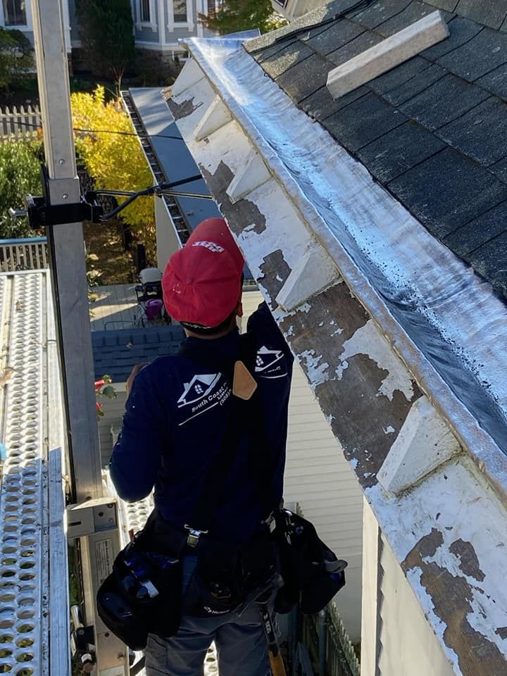 Worker on a rooftop, wearing a red hard hat, applying flashing along the roof edge.