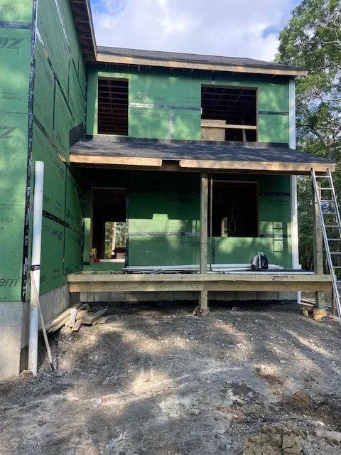 Partially built green two-story house with unfinished porch and gravel foreground