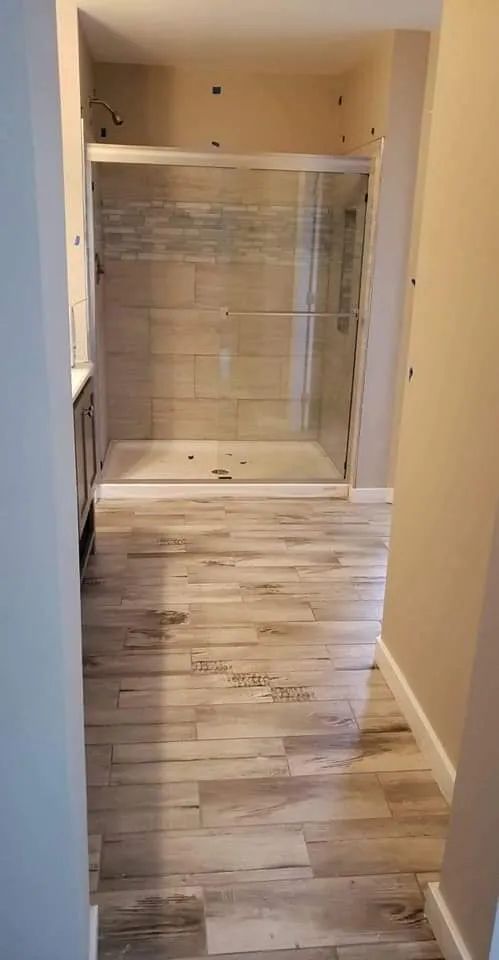 Narrow hallway leading to a tiled shower stall and closet-like built-ins in a beige interior.