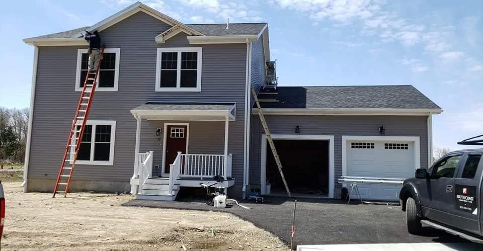 Two-story gray house with white trim, front porch, attached garage, and a ladder leaning against the upper window.
