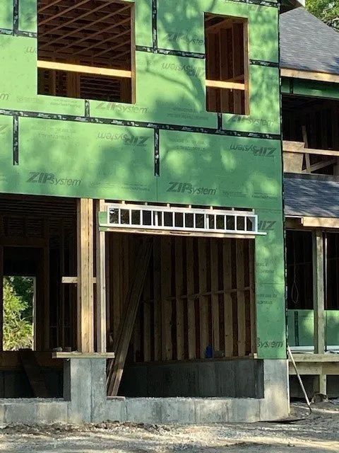 Green house under construction with exposed framing, windows, and unfinished doorway.