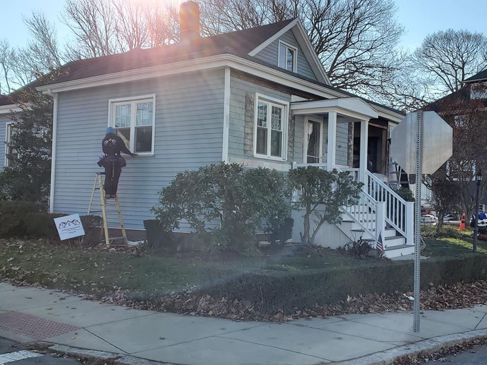 Small blue house with porch and steps, trimmed bushes, and a sidewalk in front at sunset