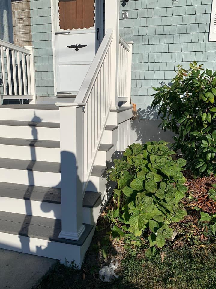 Front steps of a white house with a ramp, railing, and green shrubs beside the walkway.