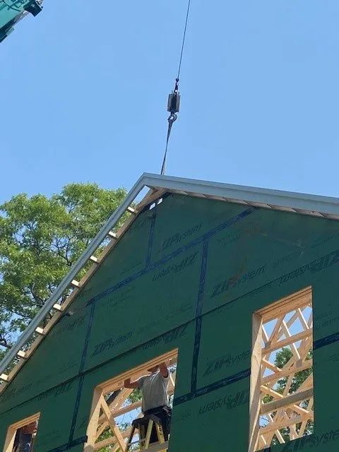 Worker installing roof on green building under a blue sky