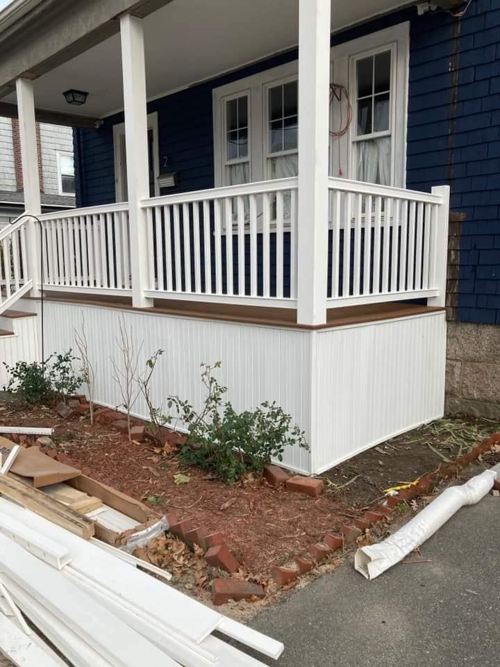 Front porch with white railing and blue siding, bordered by a small landscaped bed beside a walkway.