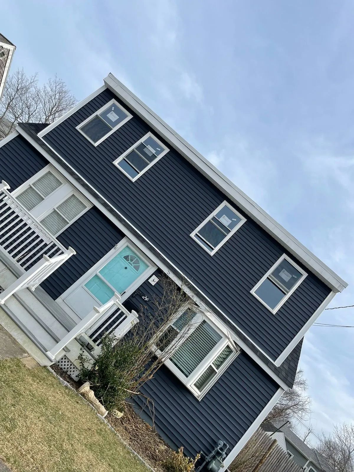 Tilted view of a dark blue house with white trim, a teal front door, and a small porch under a cloudy sky