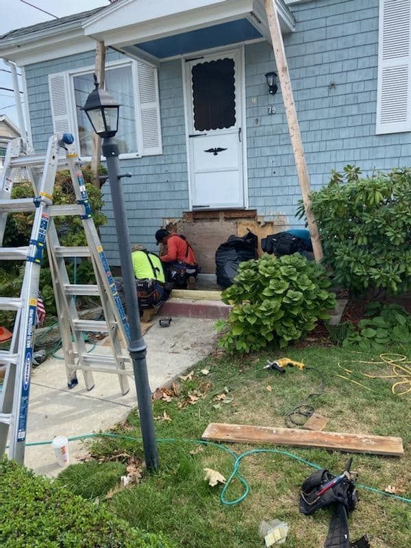 Workers repairing the front steps of a blue house beside a ladder and tools