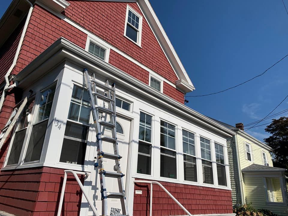 Red house with white-trimmed sunroom and ladder leaning against the side under a blue sky