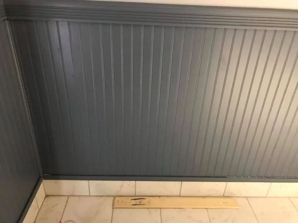 Dark gray paneled wall with a light wood floor strip and white baseboard.