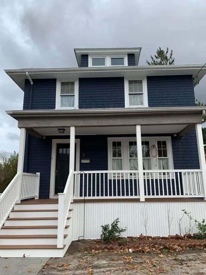 Two-story blue house with white trim and front porch on a cloudy day