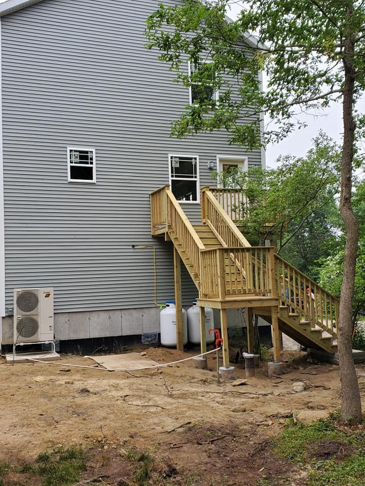 Wooden back stairs and deck on a gray-sided house, with dirt yard, trees, and an outdoor AC unit