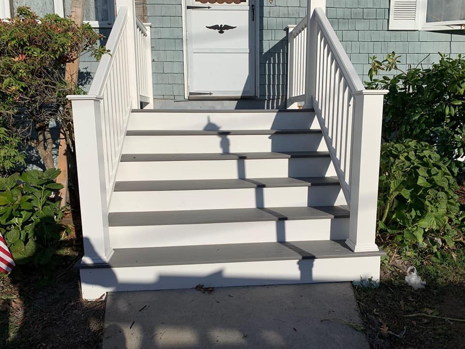 Front steps with white railings leading to a gray house entry door
