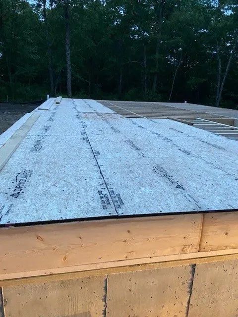 Roof underlayment on a wooden structure, viewed outdoors near a tree-lined background