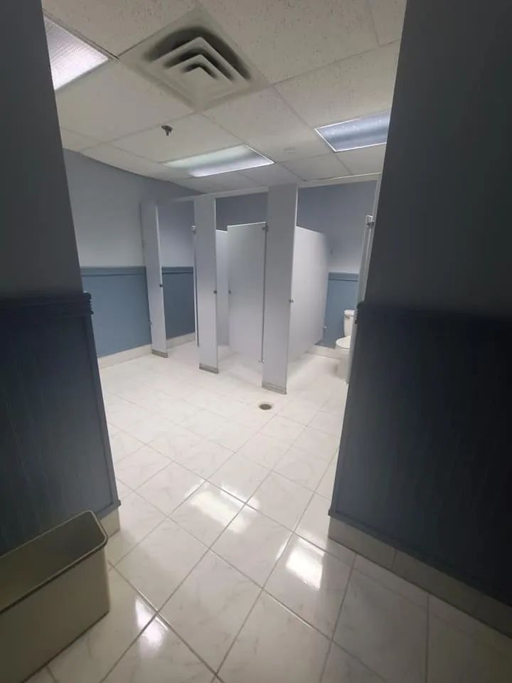 Empty restroom with white tiled floor, blue stalls, and fluorescent ceiling lights.
