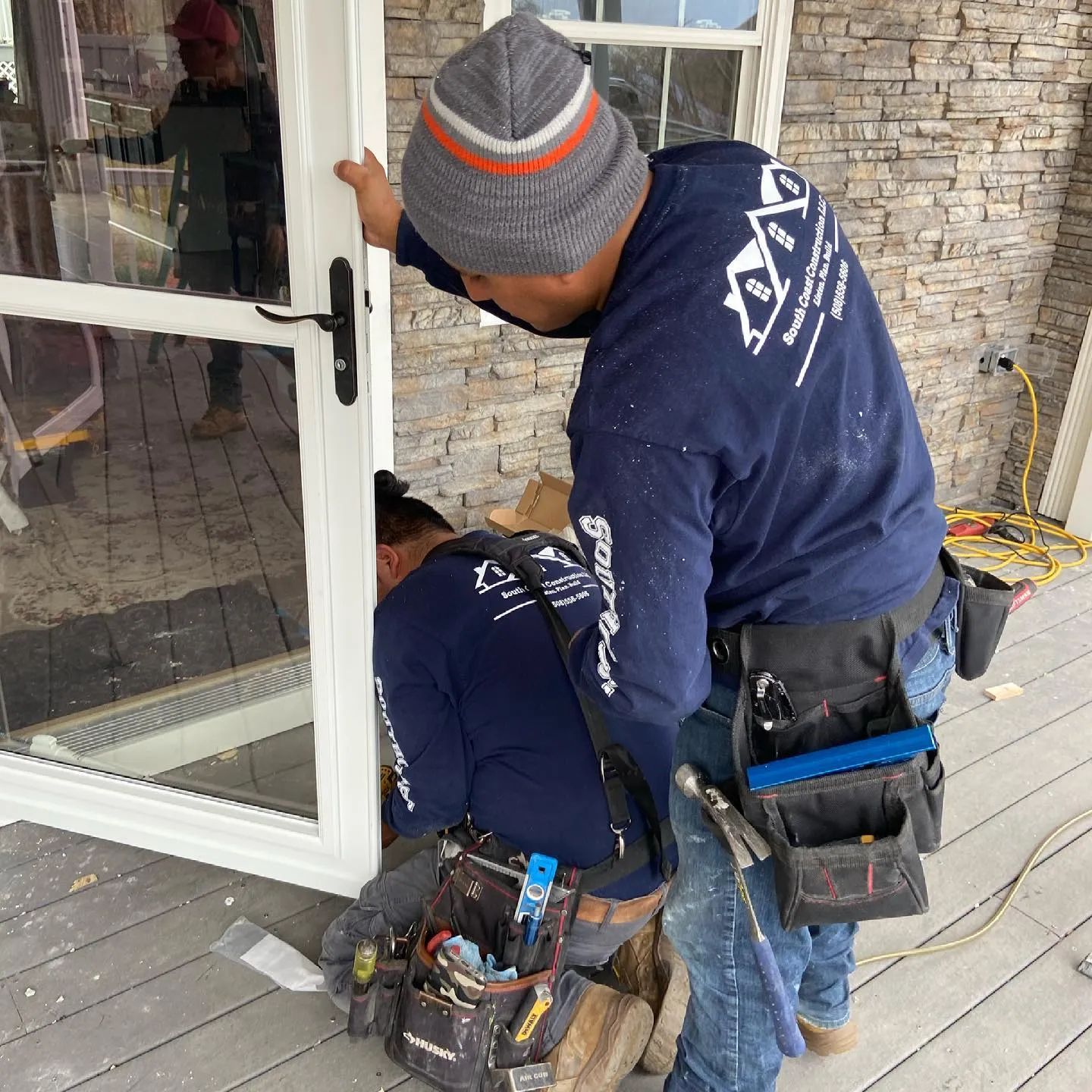 Two workers installing or repairing a white door beside a stone wall