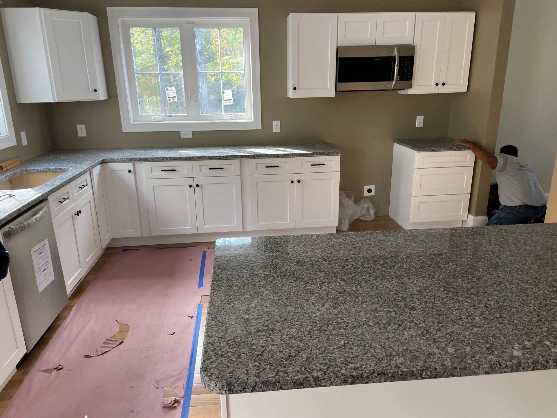 Kitchen with white cabinets, gray countertops, and a large island; floor partially covered during renovation.