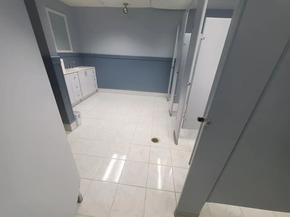 Empty tiled hallway with gray-blue walls, white cabinets, and an open doorway