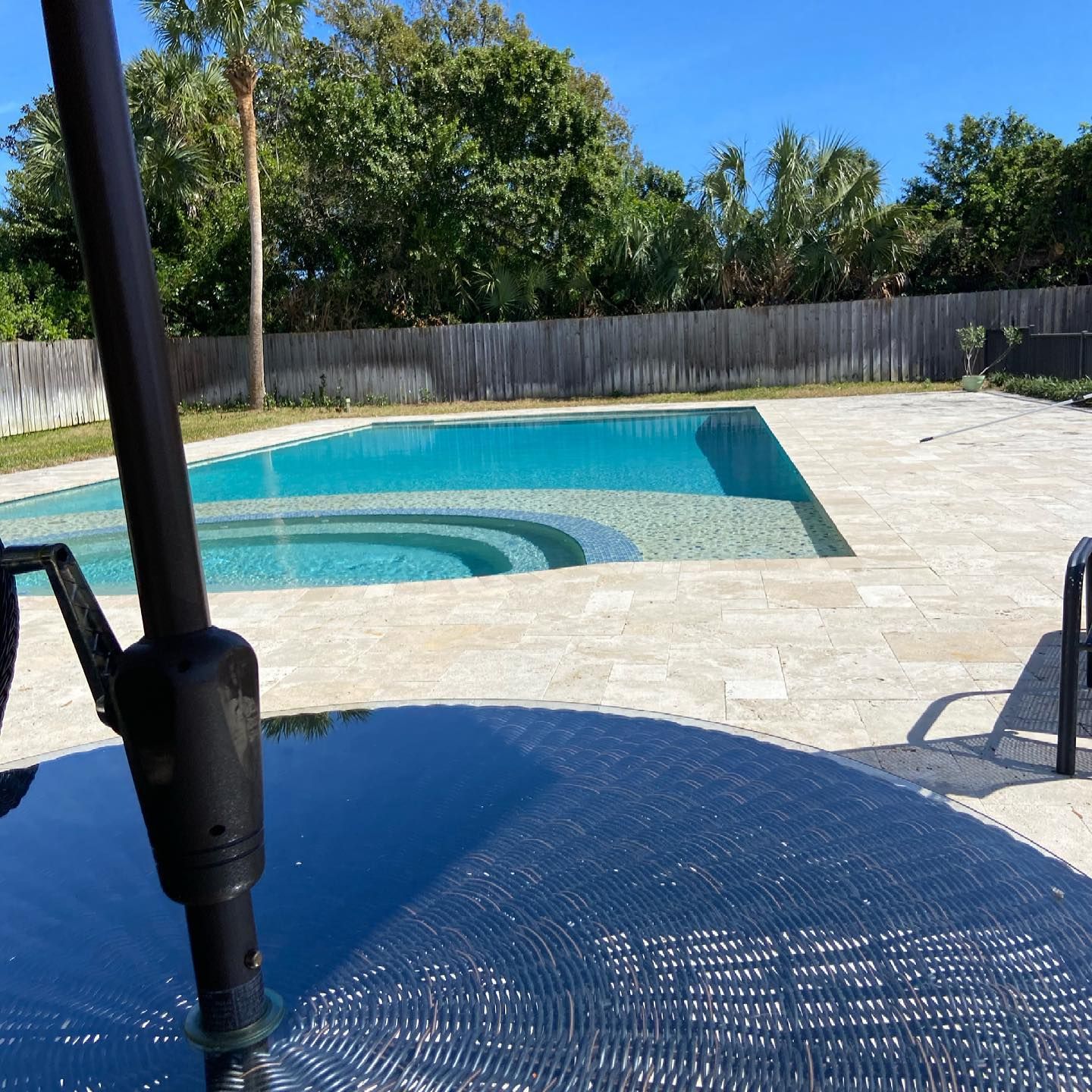 Backyard pool with blue water, stone patio, and a black umbrella stand in the foreground