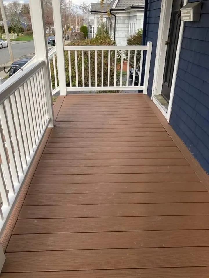 Covered front porch with brown wood flooring, white railings, and blue siding.