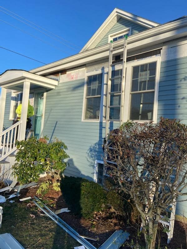 Light blue house exterior with porch, windows, shrubs, and a small garden in bright sunlight