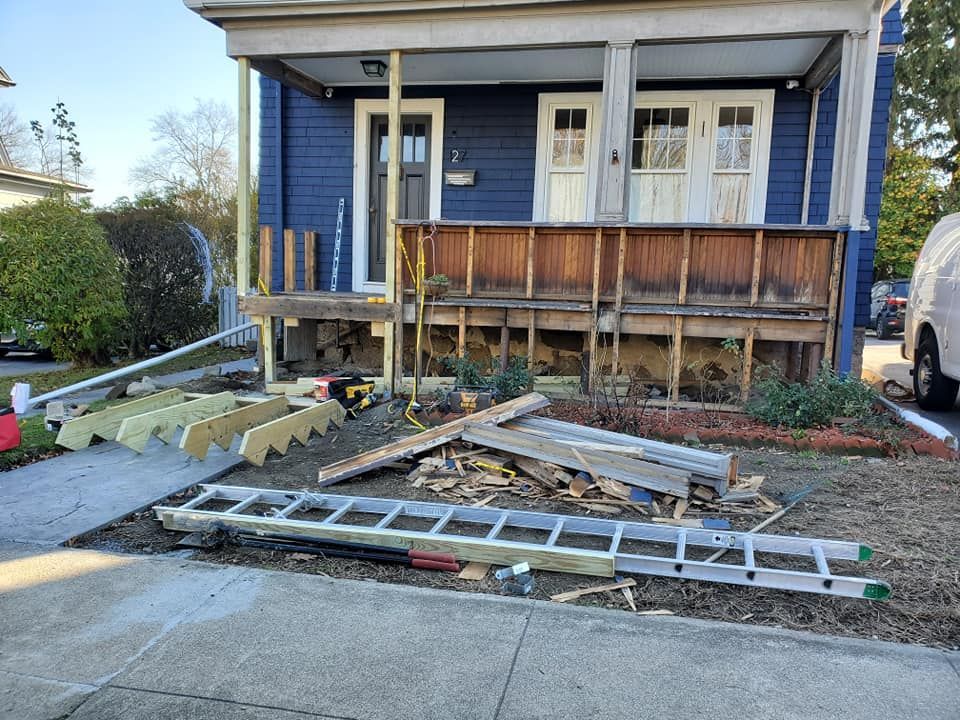 Damaged front porch with debris and ladders on the sidewalk outside a blue house
