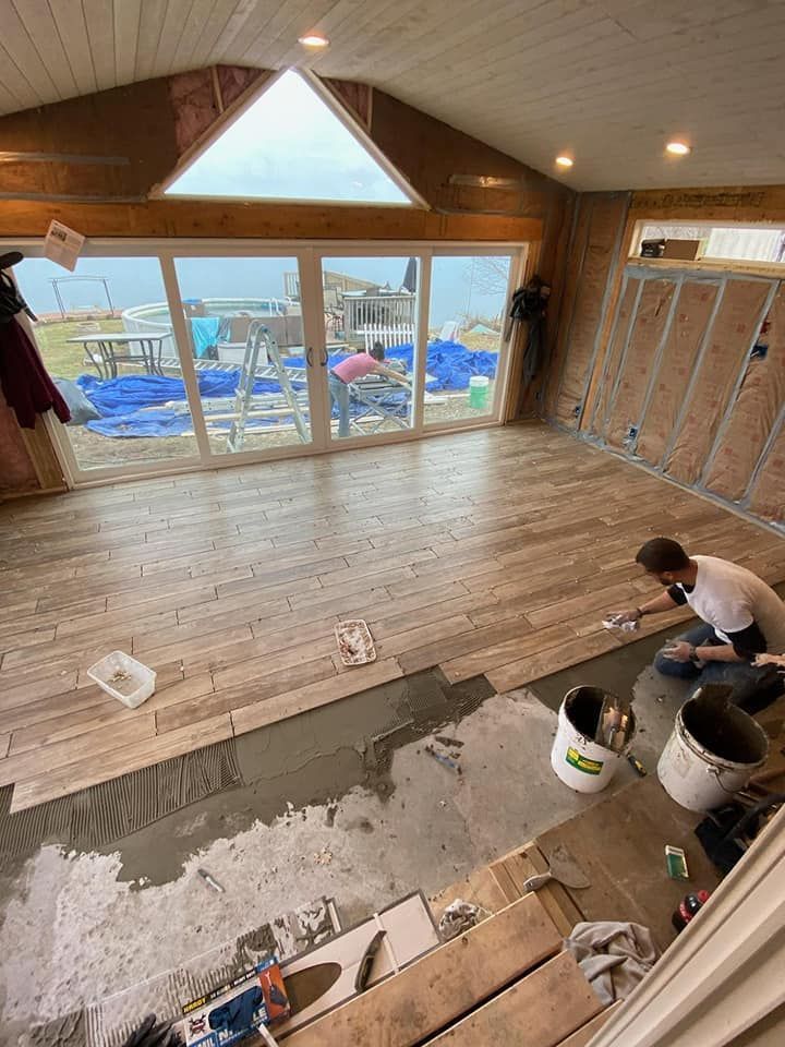 Workers refinishing a hardwood floor in a wood-paneled room with a large window and lake view.