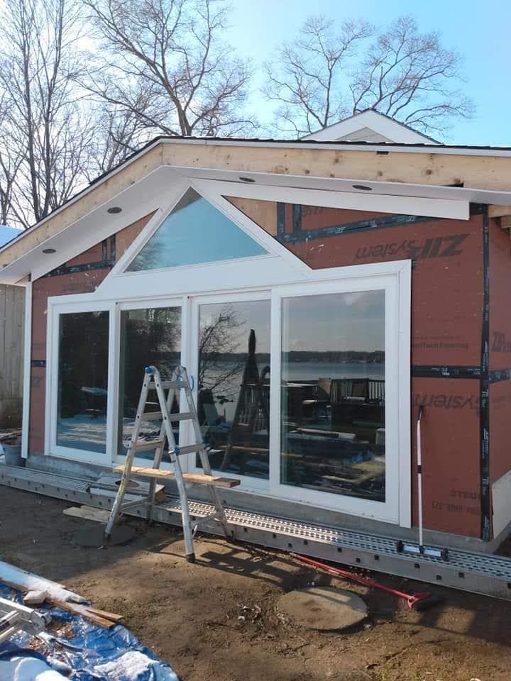 House exterior under renovation with large white-trimmed windows and a ladder in front