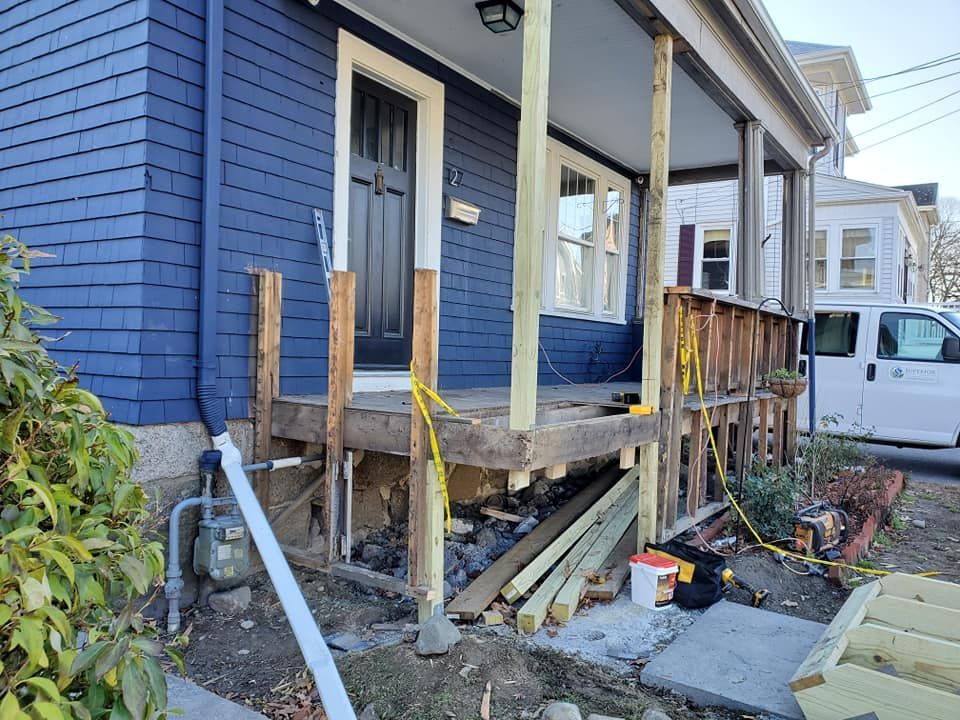 Blue house porch with missing steps, broken railings, and exposed foundation, showing structural damage
