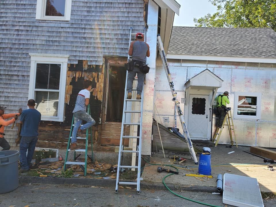 Workers on ladders repairing the exterior wall of a white building with peeling paint.