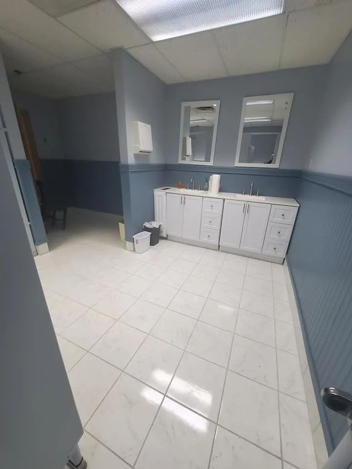Empty tiled room with blue walls, white cabinets, and two windows under fluorescent lights