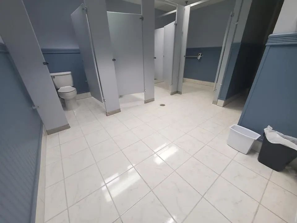 Public restroom with tiled floor, gray stall doors, and trash bins by the wall.