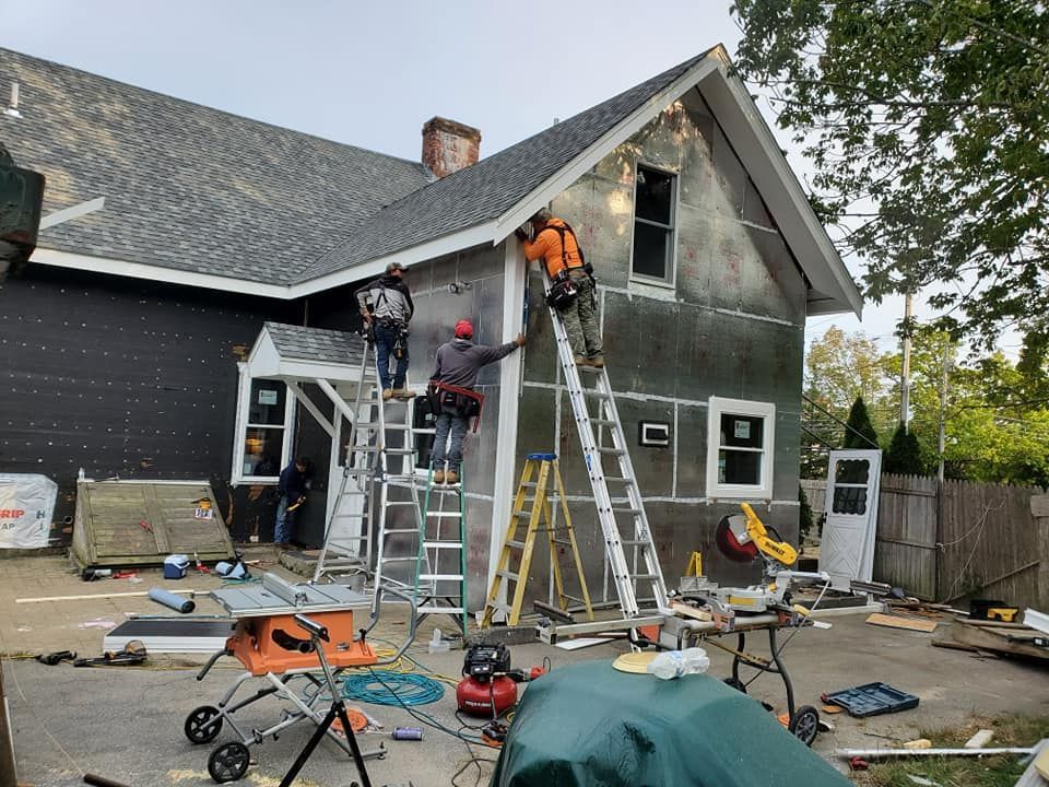 Workers repairing the front of a gray house with ladders and tools on a driveway