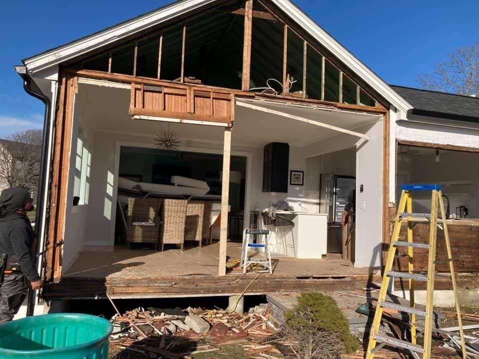 House under renovation with exposed front wall, open deck, and construction materials scattered outside