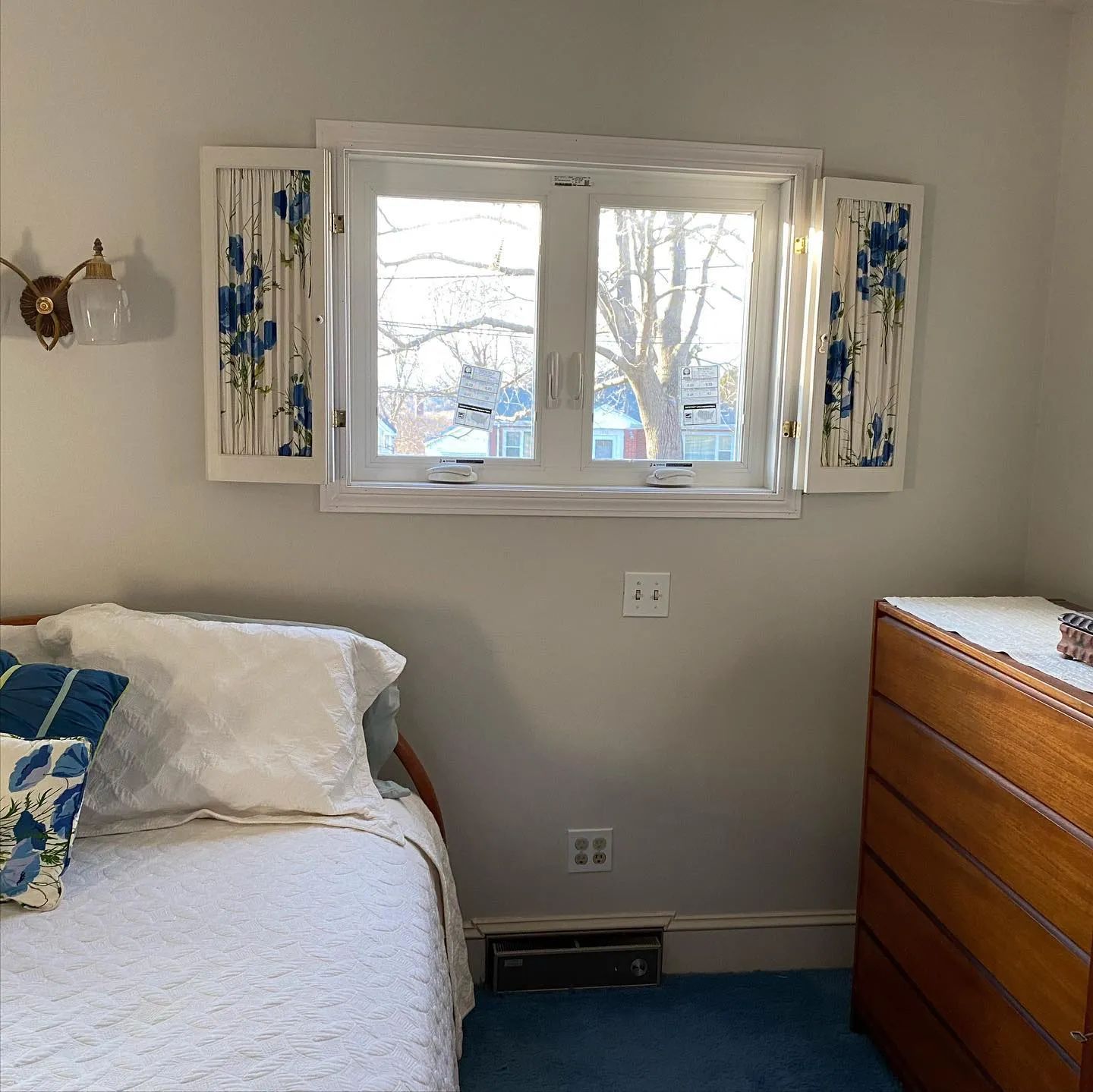 Bedroom with white bed, wooden dresser, and bright window centered on the wall