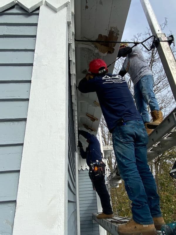 Workers in safety gear repairing the exterior eaves of a house on a ladder