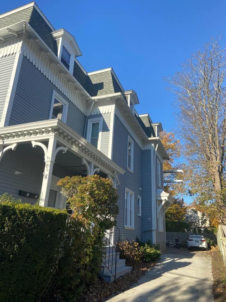 Blue Victorian-style townhouse along a sunny sidewalk with hedges and bare trees under a clear blue sky