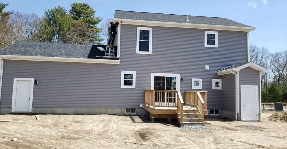 Gray two-story house with a small wooden deck and side garage under a clear sky
