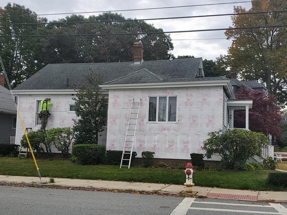 Workers painting the exterior of a white house with ladders and pink primer patches