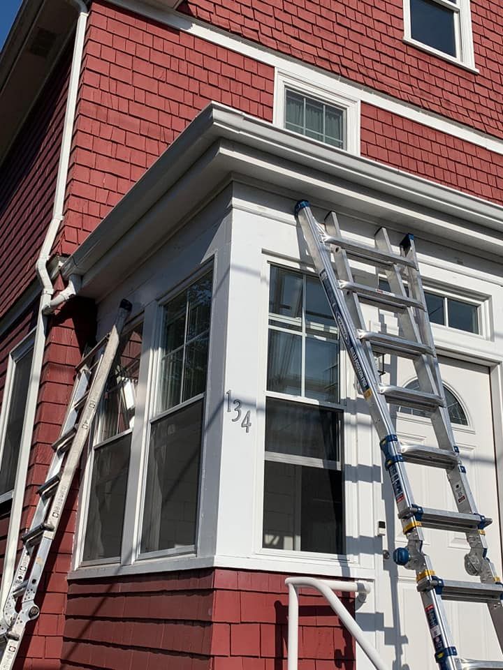 Ladder leaning against a red house with white trim around a bay window.