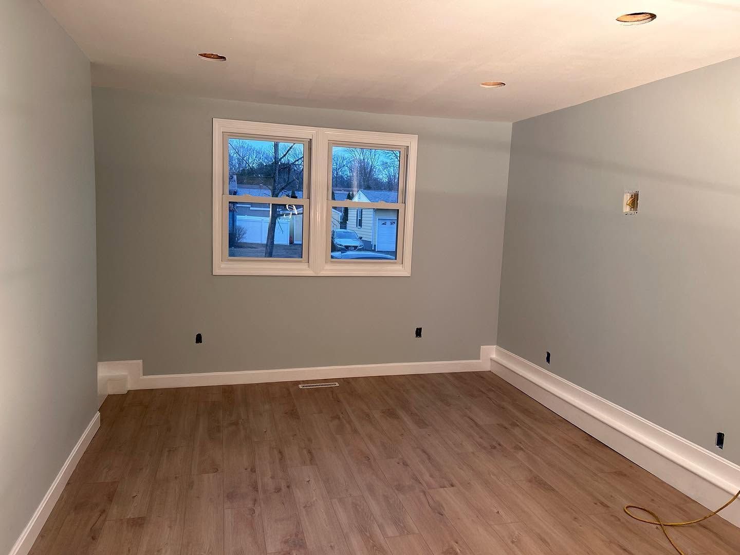 Empty room with gray walls, wood floors, and two small windows.