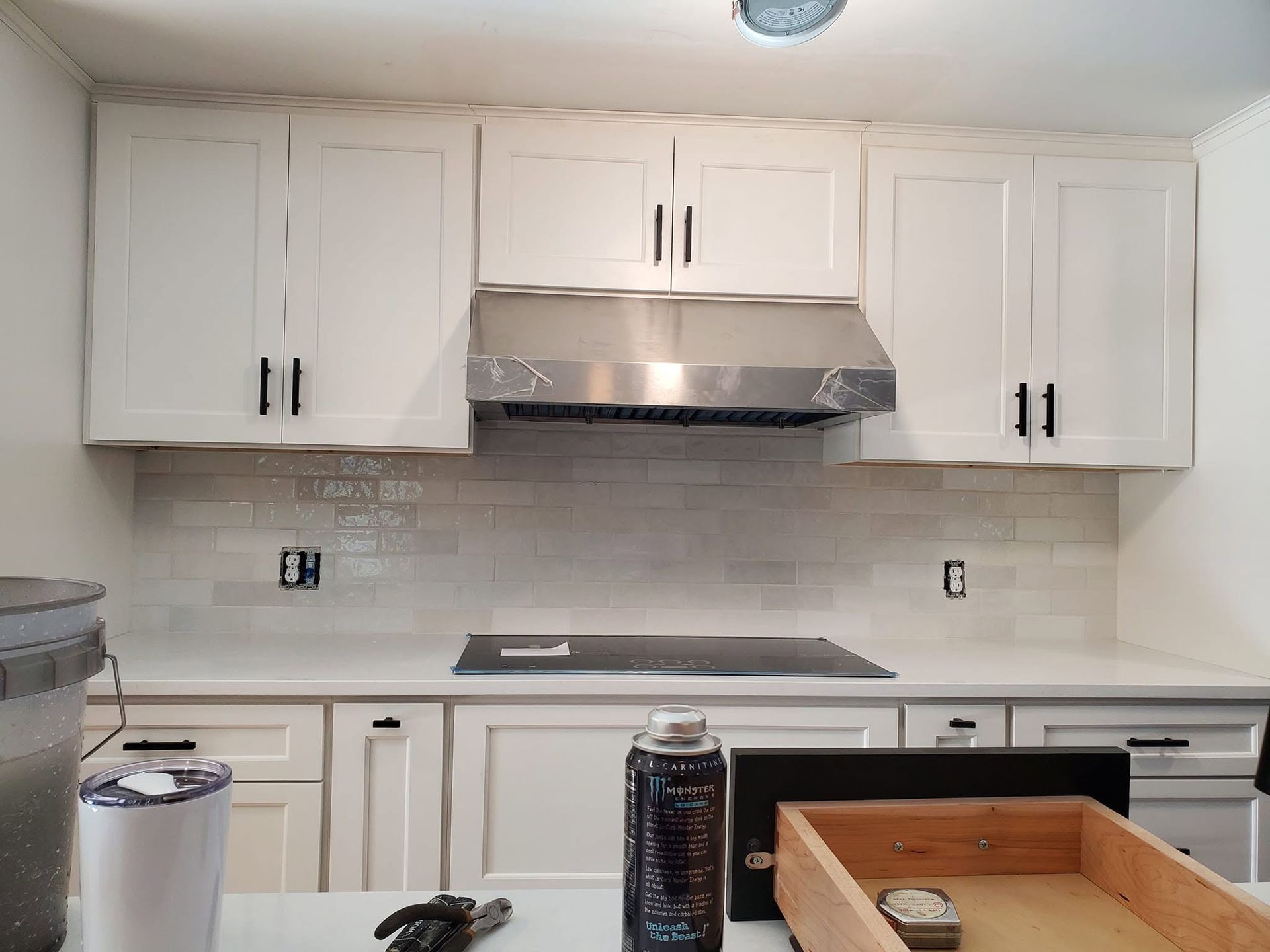 White kitchen with cabinets, stainless range hood, tiled backsplash, and countertop items in front
