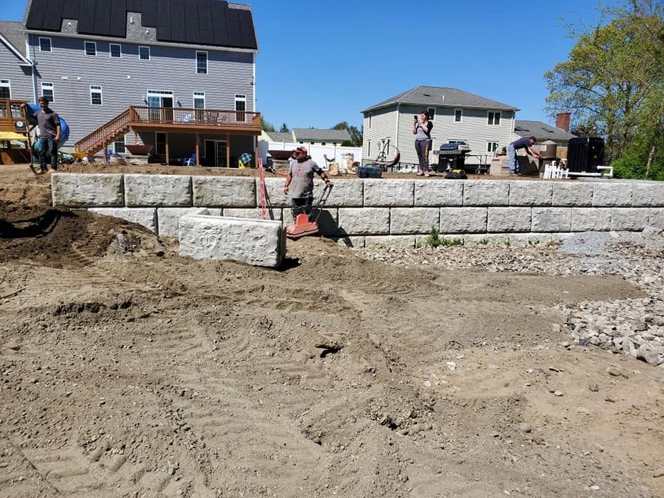Construction site with stone retaining wall, workers, and a partially built house under a clear blue sky