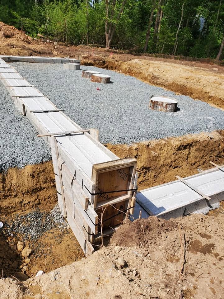 Concrete foundation footings and block formwork in a gravel excavation site surrounded by trees