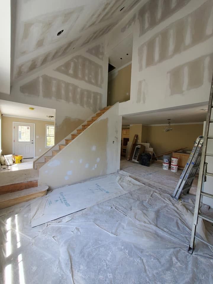 Unfinished interior with drywall, staircase, covered floor, and construction materials in a spacious room