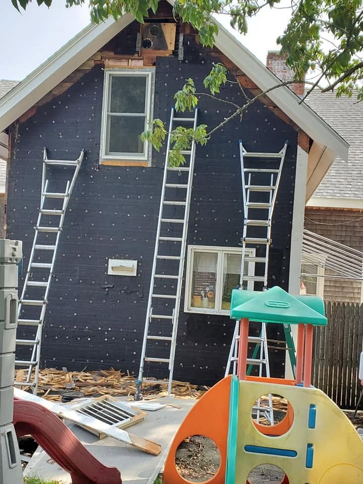 House exterior under renovation with ladders on dark siding and a children’s play structure in front