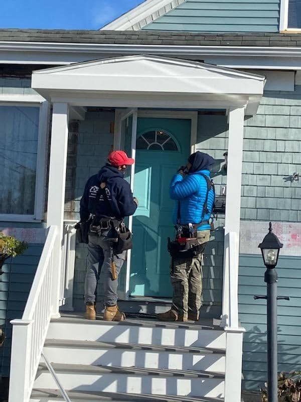 Two workers on a front porch inspecting a blue house’s front door