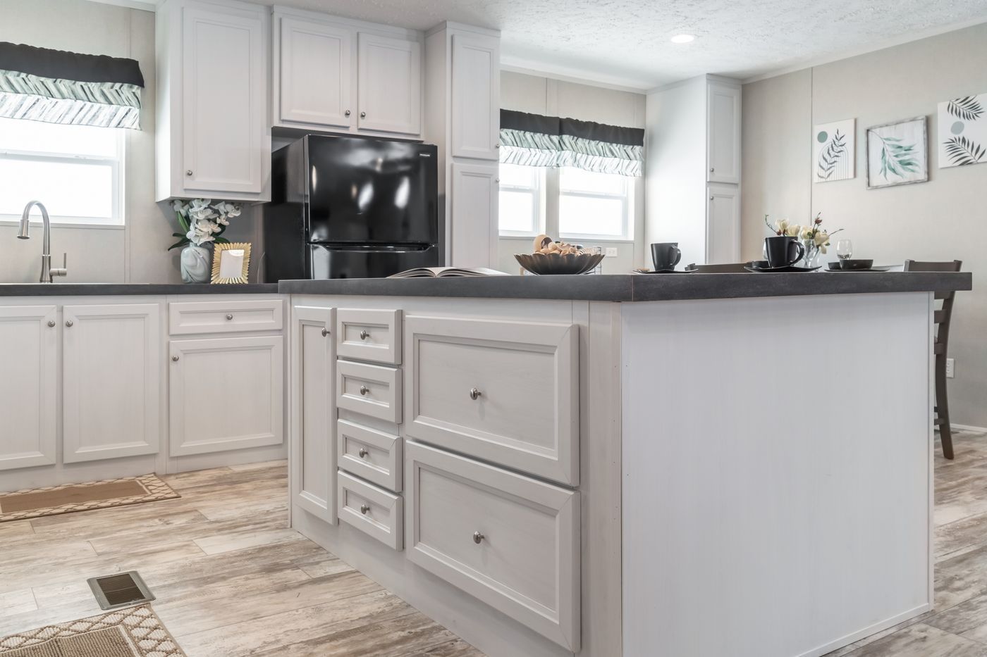 White kitchen with an island, black appliances, and light wood-look flooring.