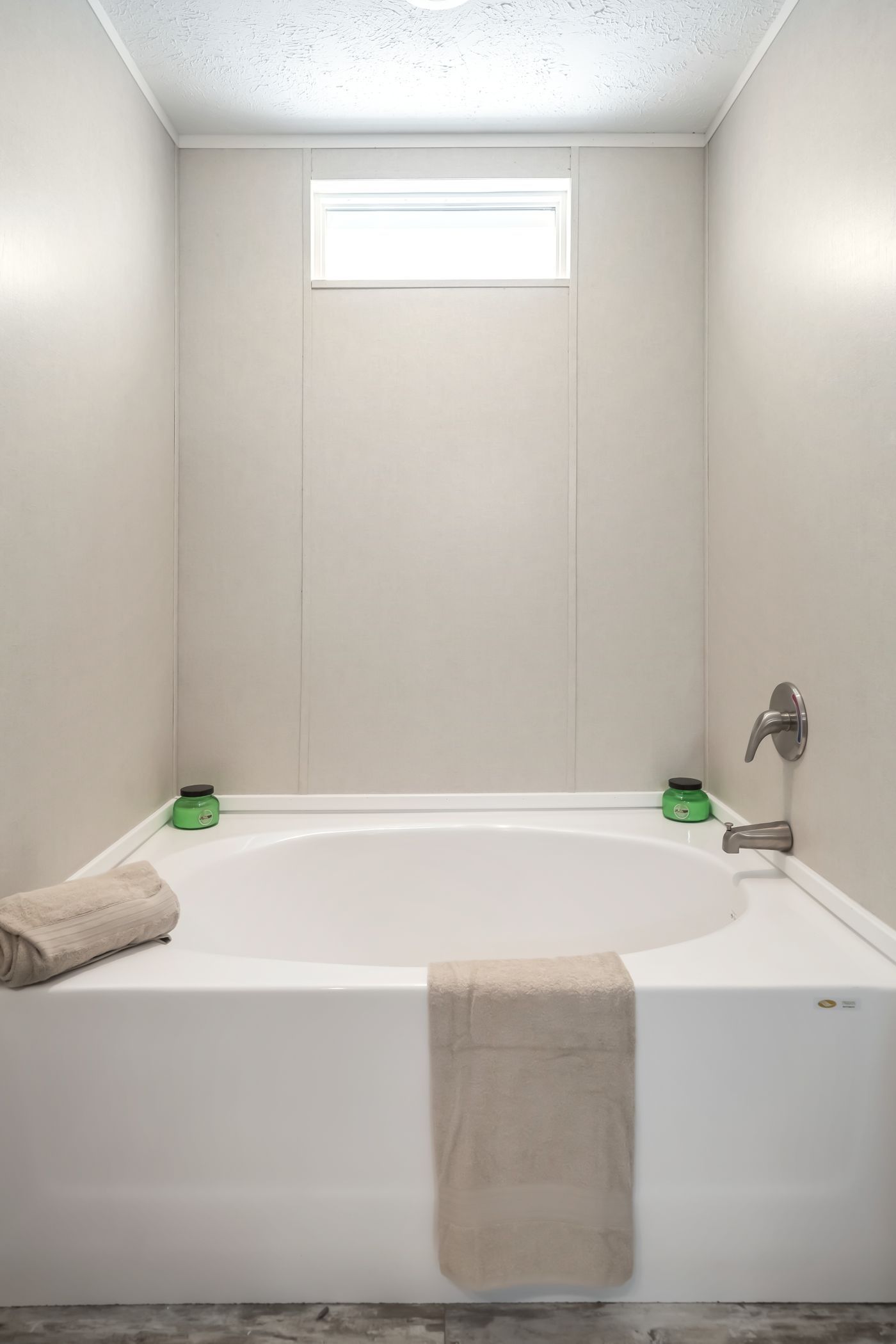White bathtub in a bathroom, with a window above. Tan towels and green soaps on the tub.