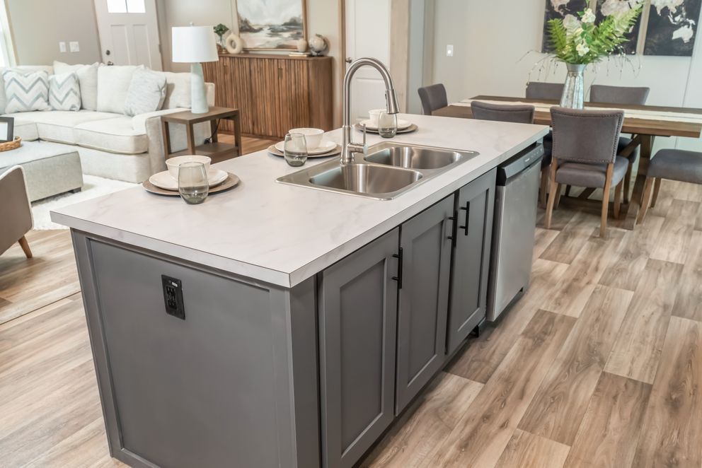 Gray kitchen island with a sink, cabinets, and dishwasher; dining area and living room visible.