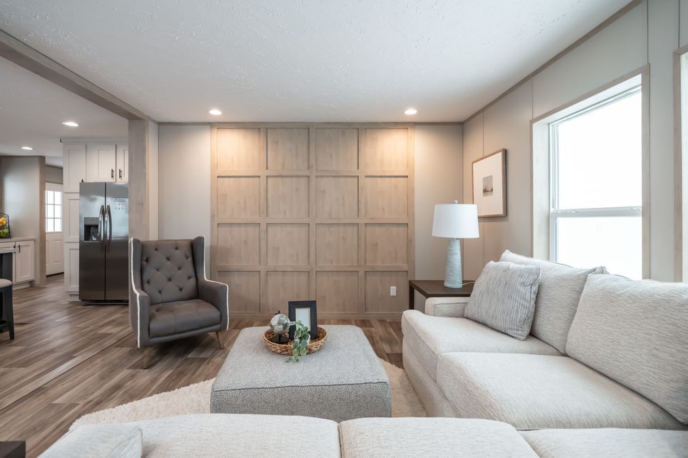 Living room with neutral tones, featuring a sofa, armchair, and decorative wall panel.